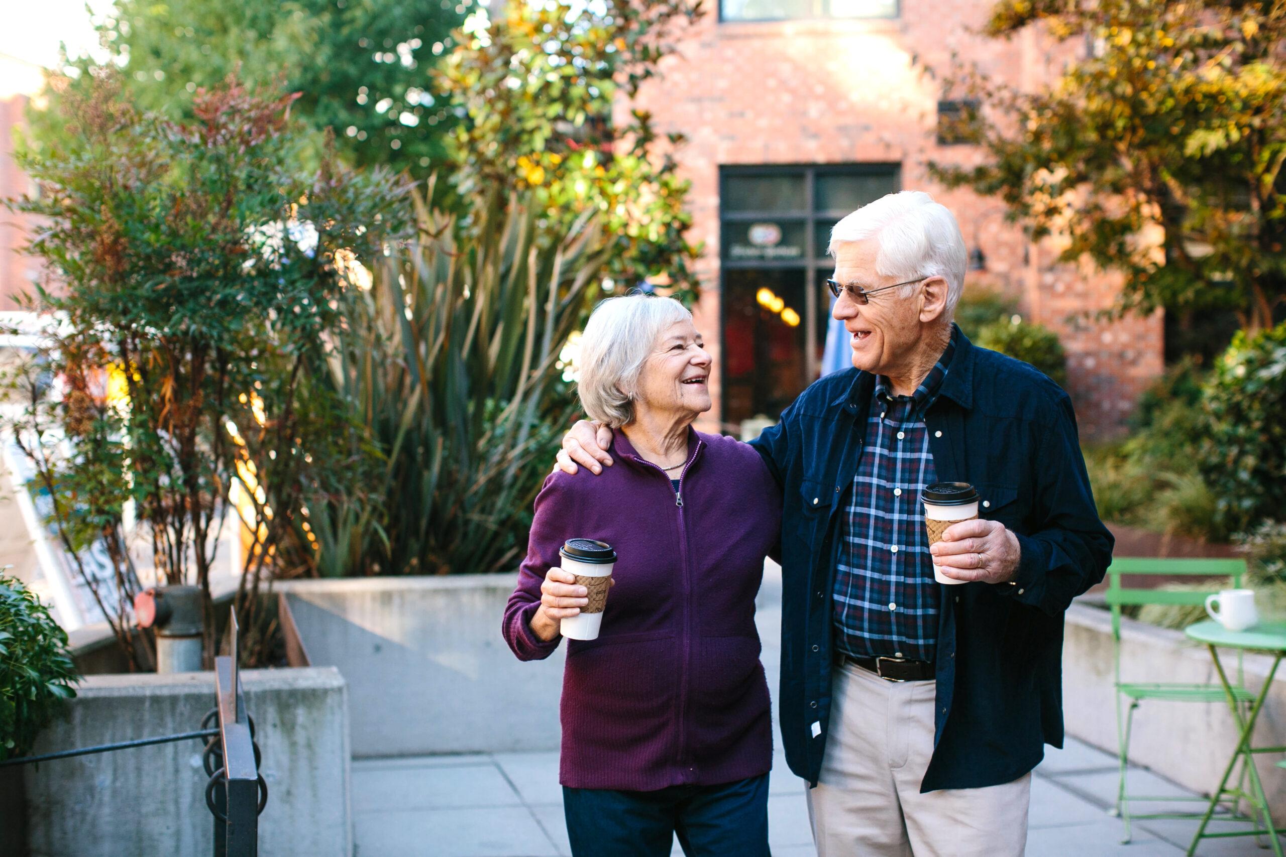 A couple smiles at each other and enjoys coffee outdoors.