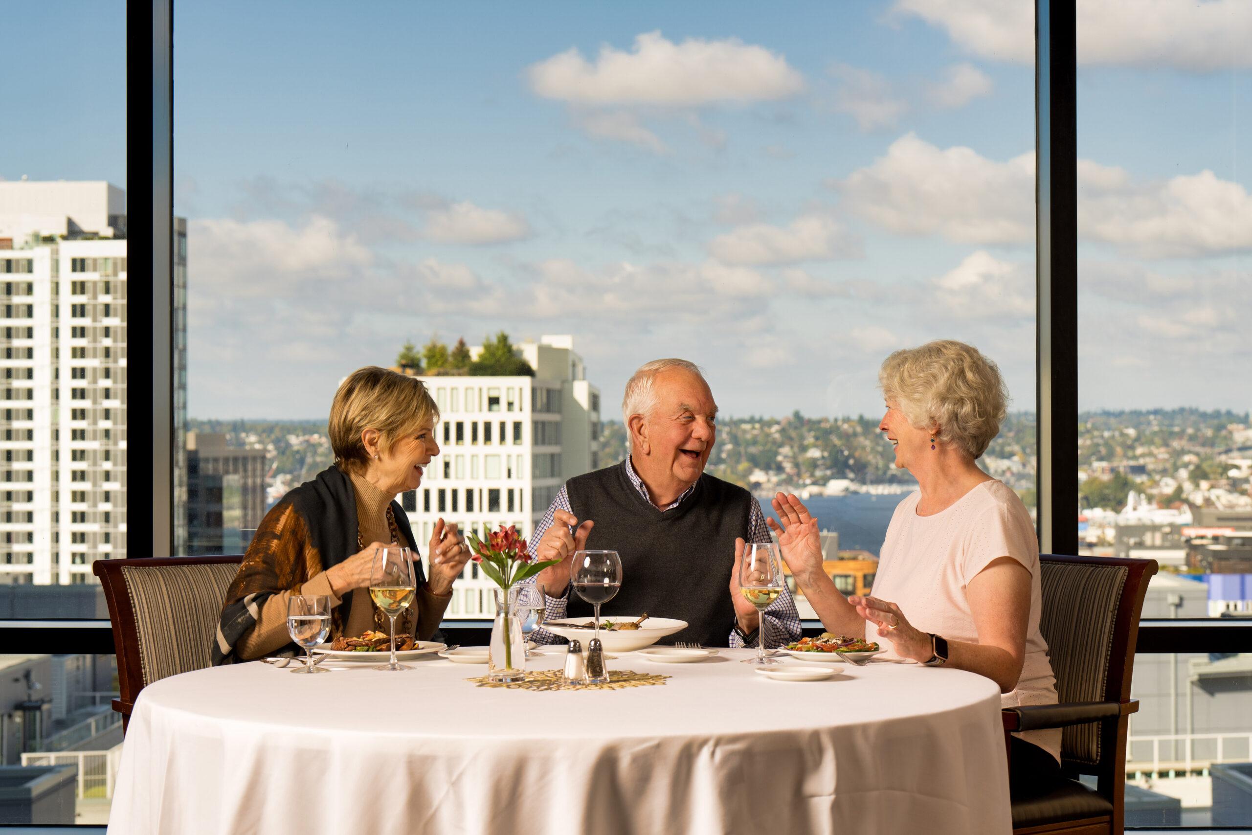 Three older adults laugh and talk at dinner.