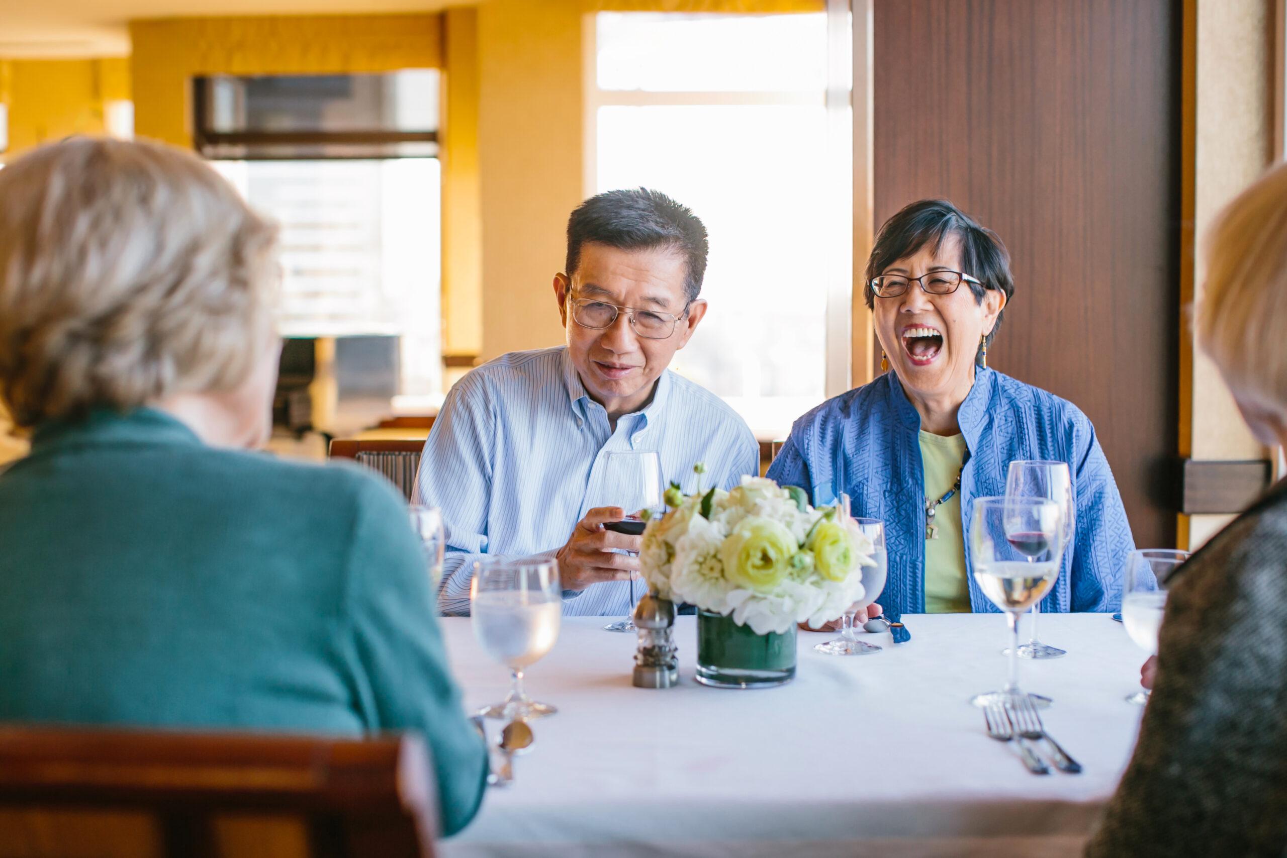 Older adults laugh and talk at dinner.