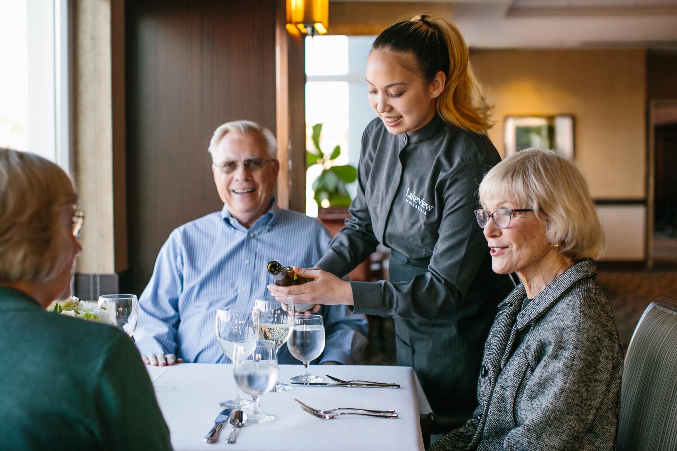 A waitress pours a glass of wine for a table of older adults.