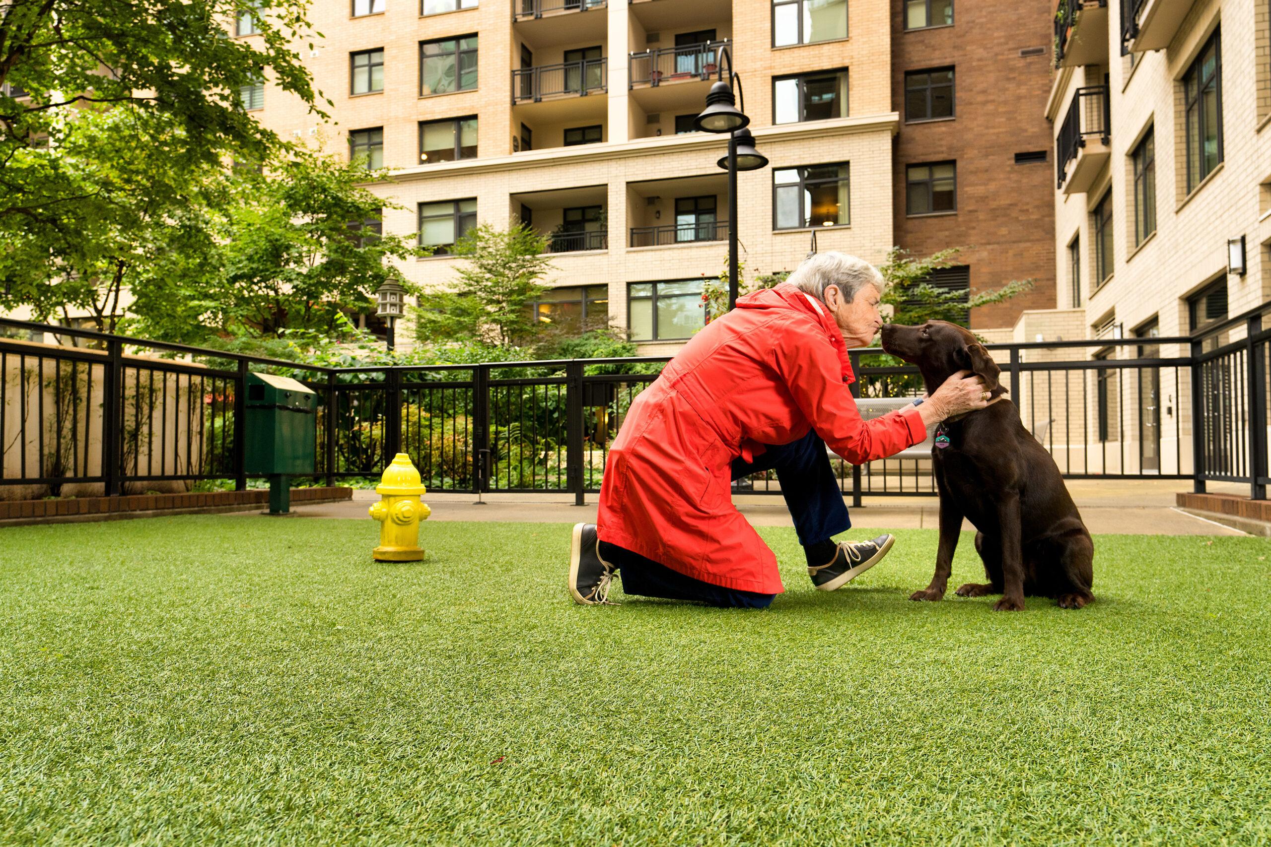 An older person wearing a red coat enjoys time outdoors with their dog.