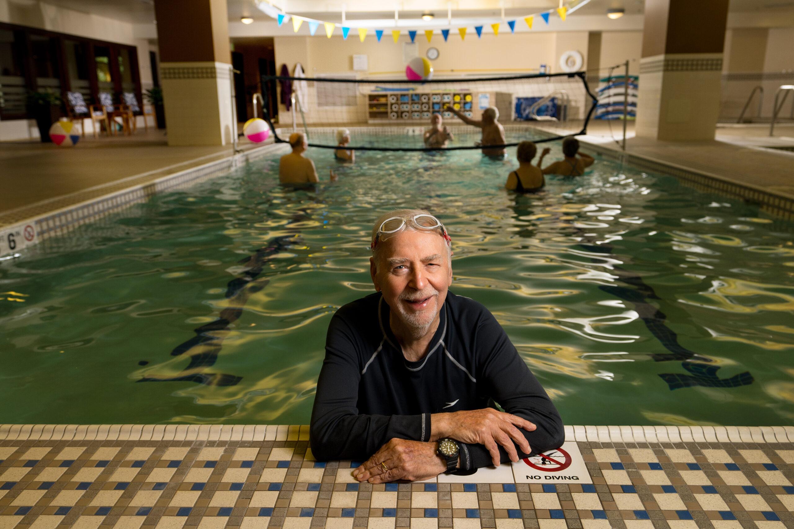 An older man smiling while resting on the side of the pool.