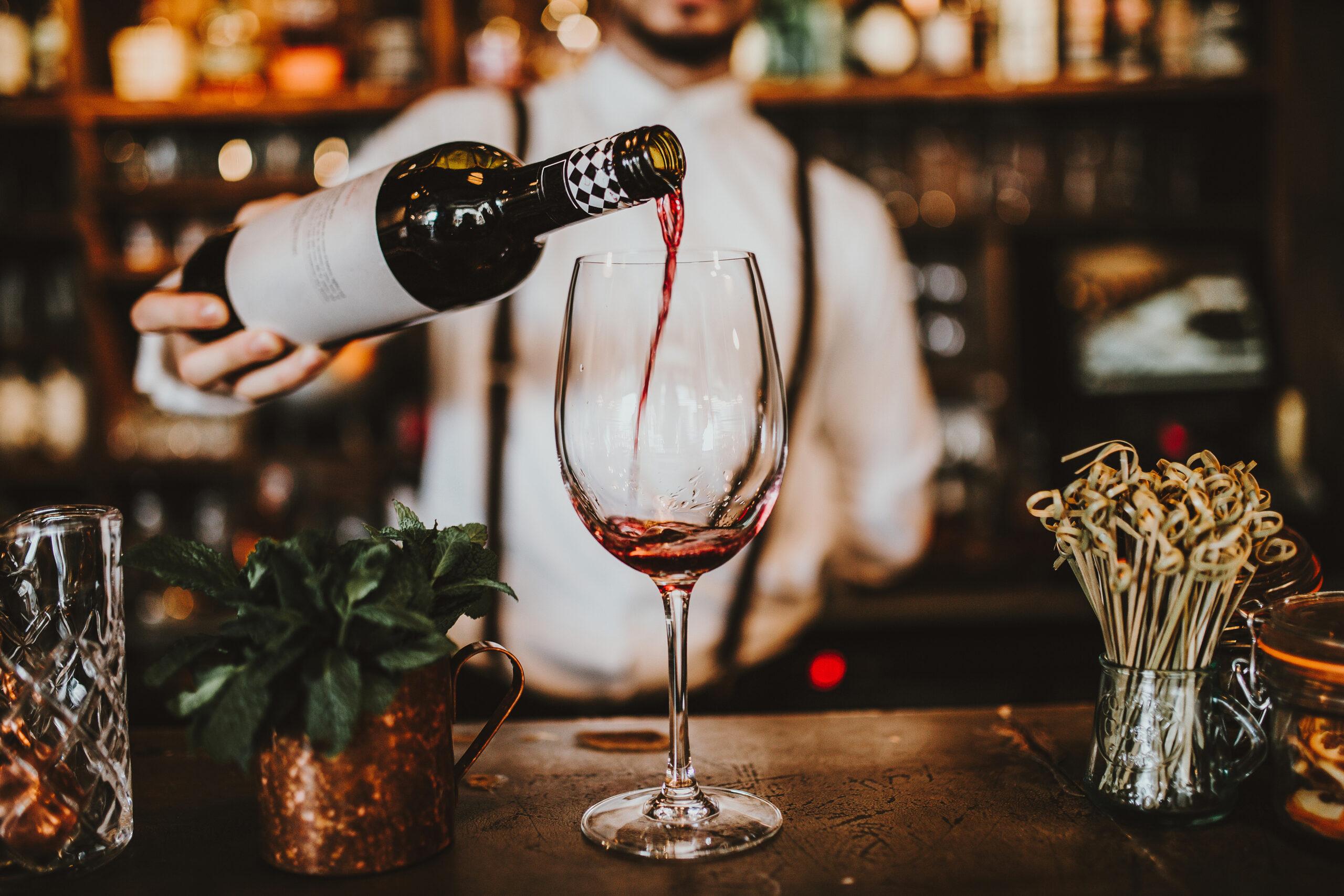 Close up shot of a bartender pouring red wine into a glass.