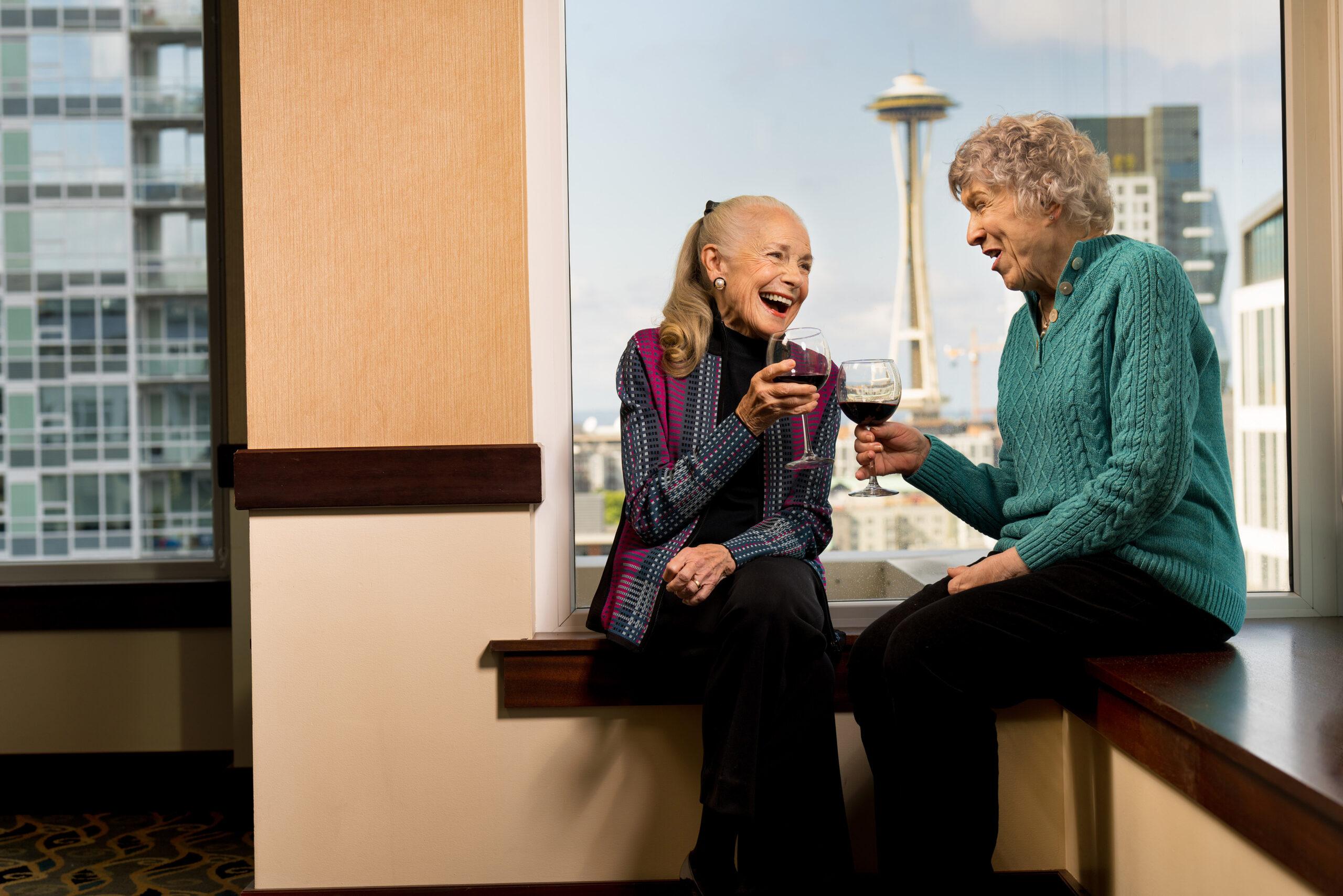 Two older women laugh and talk with glasses of wine at Mirabella Seattle.