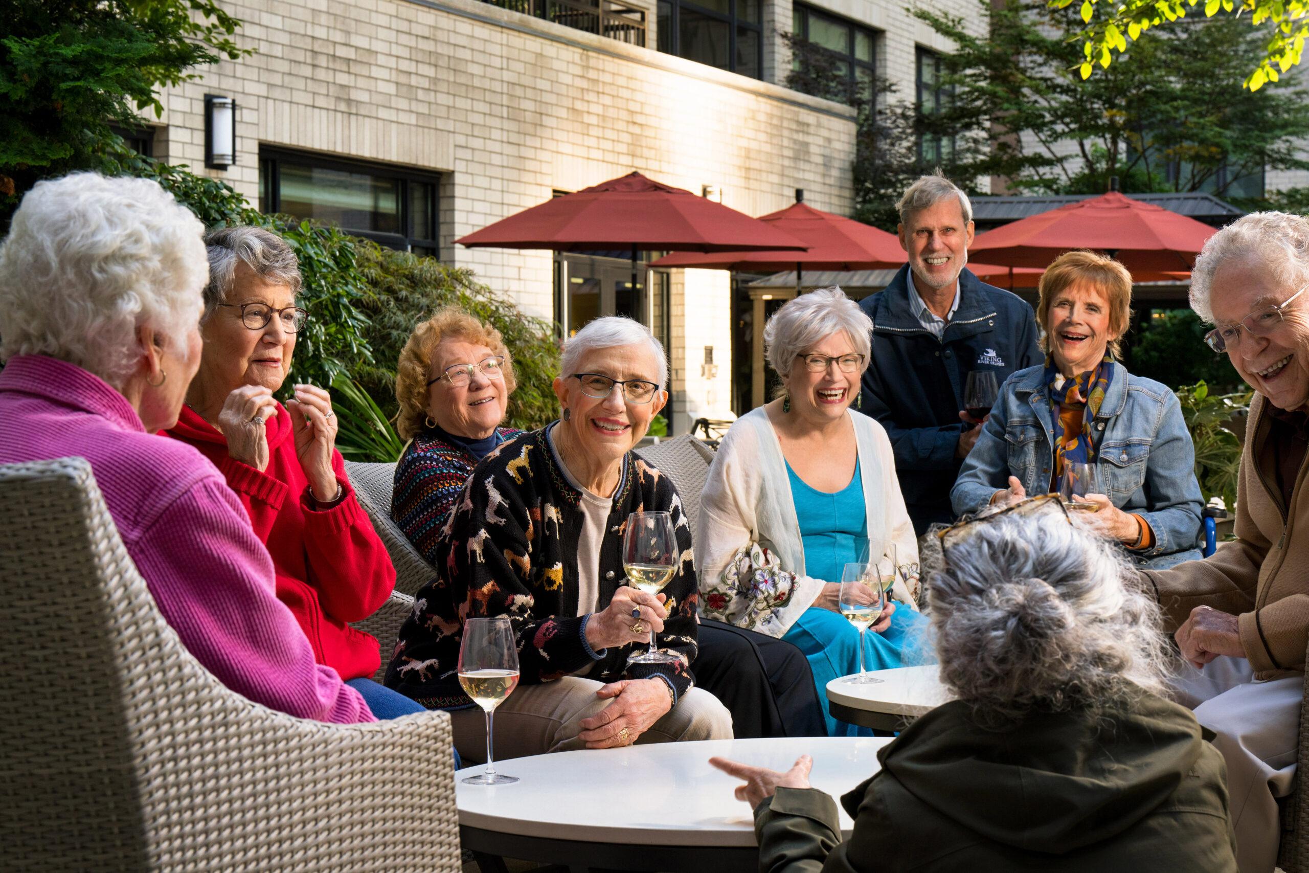 A group of Mirabella Seattle residents smiling and laughing over glasses of wine outdoors.